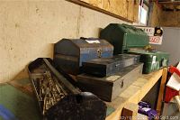 Wide view of multiple metal tool boxes in various colors arranged on a wooden shelf including green, blue, black, and silver boxes.