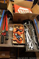 Photo showing two red handled come-along winches with hooks, orange ratchet straps, NAPA branded mat and a box containing assorted wrenches.