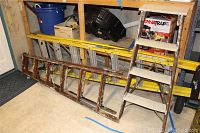 Photo showing three ladders stacked vertically against a wall: an 8-foot extension ladder, a 6-foot step ladder, and a 4-foot step ladder, all with visible wear.