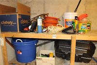 Overview of shelf containing coiled orange extension cords, propane torch kit, rope, steel wool, bucket and hard tool case.