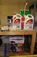 Overview of assorted bug repellents including two large Home Defense spray containers, small aerosol spray, gloves, insect net, and boxed Dynatrap XL insect trap beneath the table.