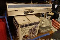 Photo showing boxed King Kooker 36 qt stainless steel boiling pot with steamer rim, lid, and basket, along with stacked disposable aluminum banquet trays and plastic platters.