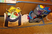 Canvas bag filled with multiple plush toys including Beanie Babies along with a yellow road sign and a large plastic Batcave tower toy positioned beside it.