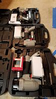 Three Porter Cable nail guns in black molded carrying cases along with boxes of nails and manuals.