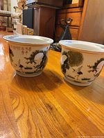 Side view of both porcelain planters displaying crane and landscape artwork