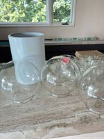 Tall white cylindrical vase, three clear glass globes, additional glass items in background