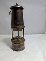 Front view of brass and steel miners safety lamp with glass globe and maker’s stamp