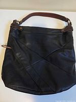 Front view of black leather bag with brown handle