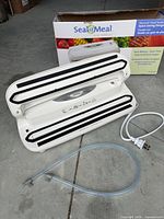 Vacuum sealer opened with hose, sealing bar, power cord and box visible