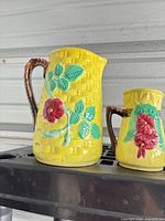 Front view of both yellow ceramic pitchers showing size difference and floral basketweave design