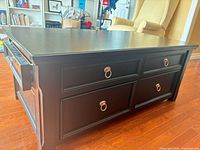 Full view of black distressed lift-top coffee table showing four drawers and side handle