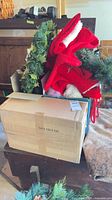 Box containing greenery, red fabric items and cardboard packaging