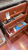 Three kitchen drawers open showing flatware, steak knives in lower drawer and box of wrap