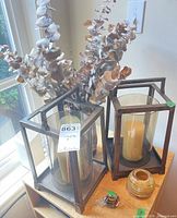 Two metal lanterns with candles, glass vase and bird on wooden surface