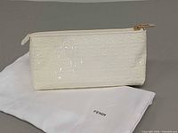 Front view of white patent leather pouch on dust bag