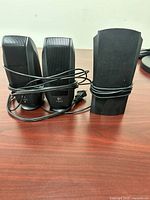 Front view of two satellite speakers and additional unit with cables