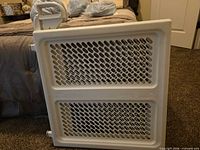 Front view of white plastic baby gate with mesh panels and handle