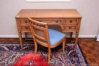 Solid wood desk and matching chair with blue seat cushion, showing the front view of both items, placed on a patterned rug.
