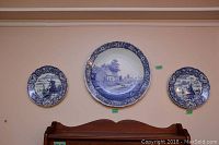 Three Delft blue and white plates mounted on wall: one large 15.75 inch plate in center and two smaller 9 inch plates flanking it.