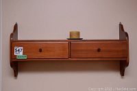 Photo of the wooden wall-mounted shelf with two drawers, candle, and metal plate on top, showing front view.