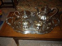 Full view of silverplate tea service including tray, coffee pot, tea pot, creamer, and sugar bowl arranged on wooden table.