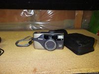 Nikon 1251 camera with wrist strap and black soft carrying case on a wooden surface.