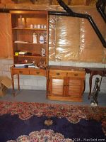 Wide view showing desk with bookcase on top and cupboard next to it in basement environment with rug in foreground.