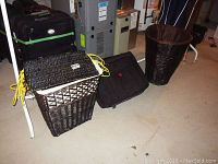 Photo showing two black wicker hampers and one black soft fabric luggage bag on a concrete floor near a utility panel.