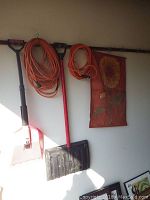 Photo of garden hoe, snow shovel, two orange extension cords hanging on hooks against a white wall