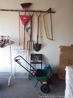 Full view of gardening tools hanging on wall above a black foldable chair and Scotts Turf Builder spreader on floor with potting soil bags nearby.