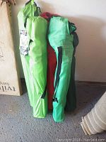 Four folding camping chairs in different colored carry bags standing upright on a floor against a wall.