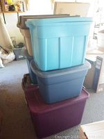 Stacked plastic storage bins of five different colors in garage setting, showing various sizes and lids.