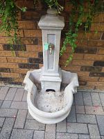 Photo of full front view of the outdoor water fountain showing the vertical rectangular body with spigot and scalloped basin base.