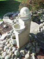 Outdoor fountain situated in garden surrounded by stones and plants, showing full vertical height and surroundings.