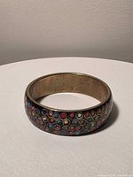 Side view of cloisonné bangle showing multicolour circular mosaic and brass interior