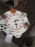 Front view of white kids sports theme wall clock showing sports ball graphics and clock face