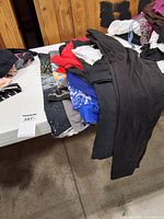 Stacked garments on table including black pants, red sweater, blue top, Star Wars tee