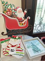 All items together: metal Santa sleigh sign, two Santa stockings, framed print