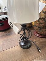 Full view of lamp showing metal base, twisted stem, white drum shade, power cord with plug