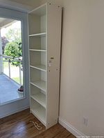 Front view of tall white laminate bookcase beside window