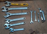 Group of six adjustable and five fixed wrenches laid out on workbench