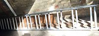 Full view of aluminum extension ladder lying horizontally against brick wall