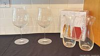 Two Riedel wine glasses alongside two Monchego carafes with box