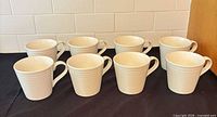 Eight white ribbed mugs displayed in two rows on dark cloth
