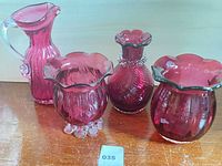 All four cranberry glass pieces grouped on surface