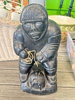 Front view of black soapstone carving showing Inuit hunter with rope and seal at base