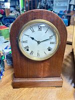 Front view of wood arch-top mantel clock showing brass bezel, dial, hands and numerals