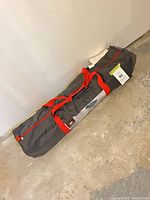 Gray bag with red straps containing cot placed on floor
