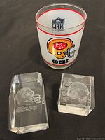 Group shot of one frosted 49ers glass and two crystal paperweights
