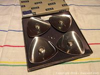 Four triangular stainless steel candle holders in open box